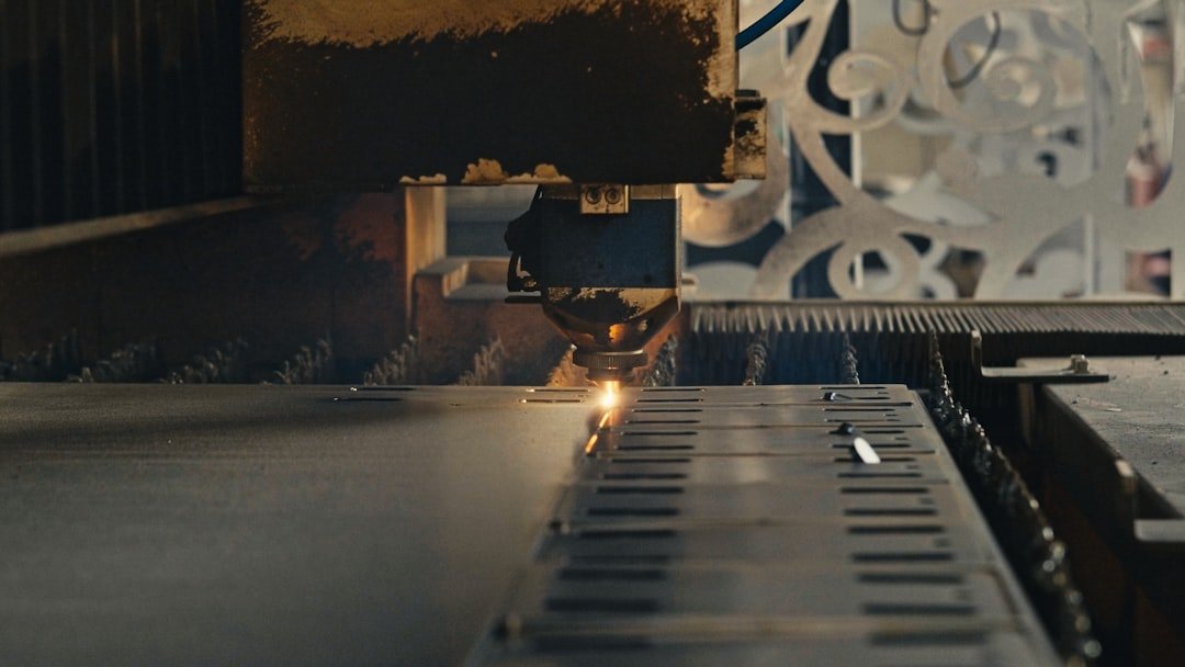 A laser cutting machine precisely engraves a metal sheet, creating intricate patterns. The image showcases advanced industrial technology and precision in metal fabrication.